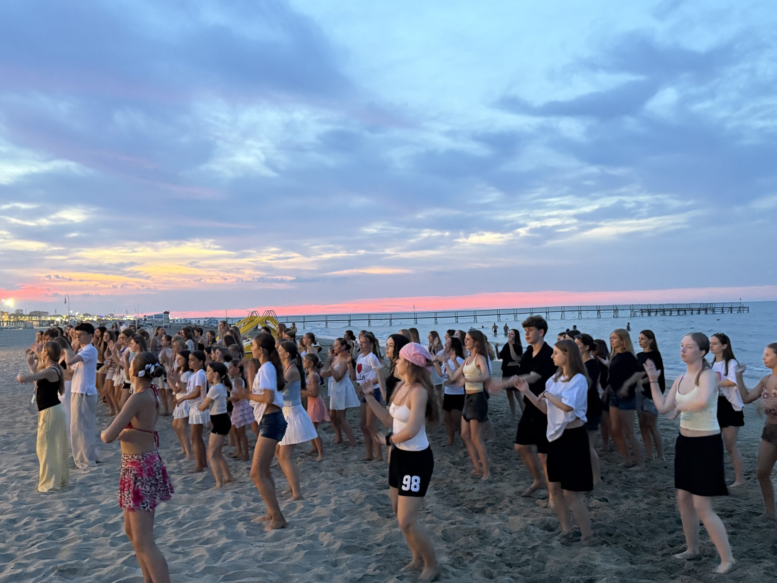 Uczestnicy Top Art Festival tańczący wspólnie na plaży o zachodzie słońca